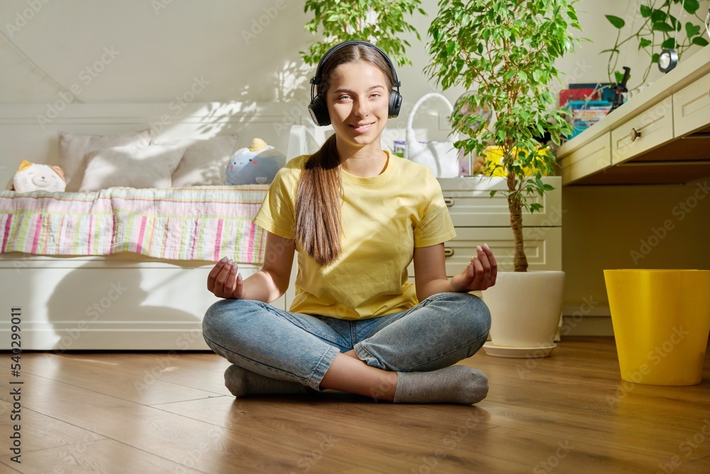 Teenage girl in headphones relaxing, sitting in lotus position at home