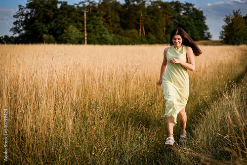 Fotografie a beautiful girl with long dark hair in a light green dress runs through a field