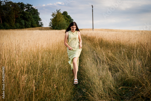 a beautiful girl with long dark hair in a light green dress runs through a field on a summer evening photo