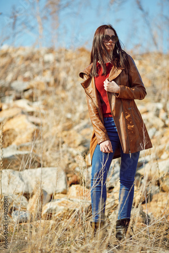 Outdoor portrait of beautiful woman in leather jacket and sunglasses against rocks background