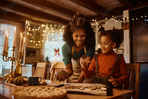 Happy black mother and daughter enjoy in making holiday cookies in kitchen.