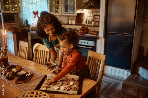 African American little girl and her mother baking Christmas cookies in kitchen.