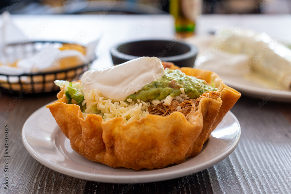 A crisp Mexican taco bowl made with a round baked tortilla shell filled with beans, corn, beef, sour cream, guacamole, avocado, lime, onions, tomatoes, shredded cheese, spicy salsa, and green lettuce A crisp Mexican taco bowl made with a round baked tortilla shell filled with beans, corn, beef, sour cream, guacamole, avocado, lime, onions, tomatoes, shredded cheese, spicy salsa, and green lettuce