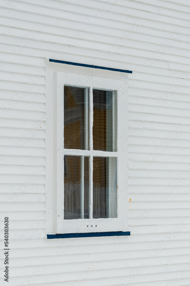 A small single casement window in a white narrow wood beveled clapboard siding exterior wall of a vintage house. The glass window has four panes with green narrow decorative trim on the outside edge. A small single casement window in a white narrow wood beveled clapboard siding exterior wall of a vintage house. The glass window has four panes with green narrow decorative trim on the outside edge.