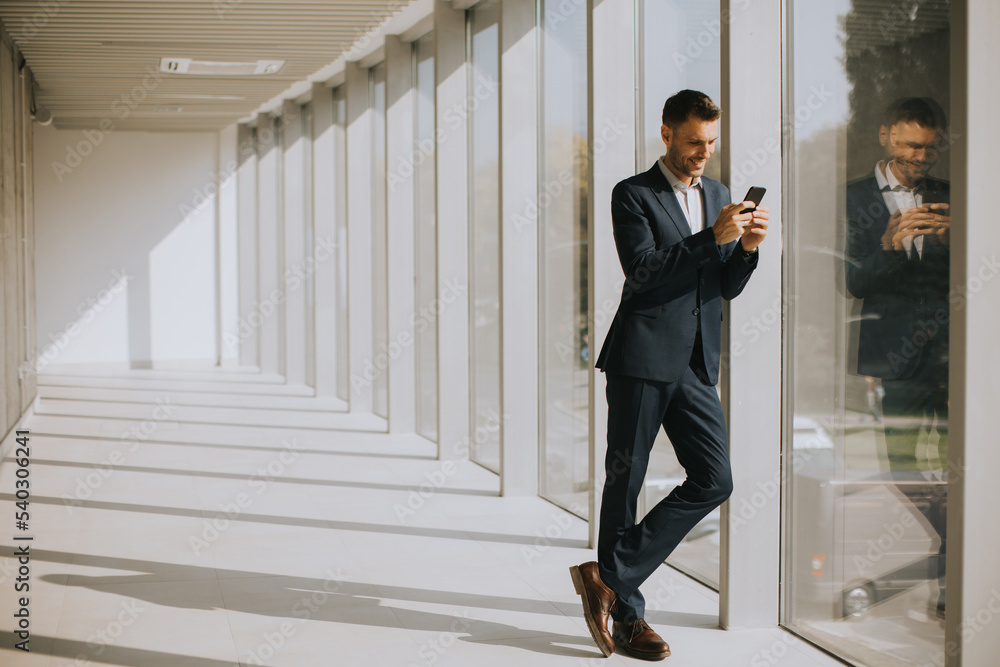 Young business man using mobile phone in the modern office hallway
