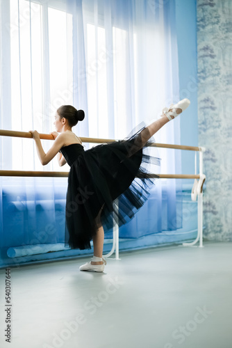 A beautiful girl ballerina in a black dress is engaged at the stonk. She's in a dance studio. Beauty. Dancing. Creation.