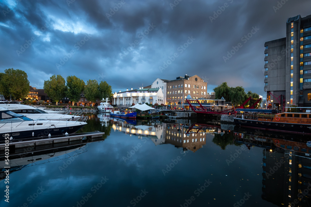 Boats in marina with restaurants and hotels in a modern city. London, United Kingdom. Travel Destination. Night after cloudy sunset.