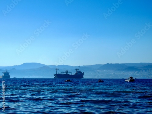 A wide landscape shot of the sea with ships passing by and a mountain range in the background © Cee