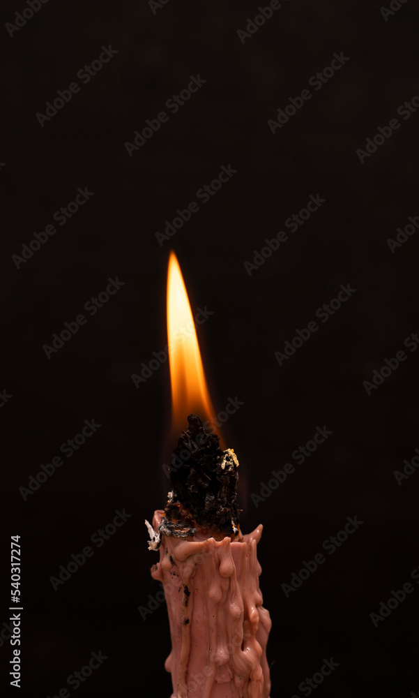 Naklejka premium Wax candle with a handmade twist of natural herbs. The candle burns on a black background.