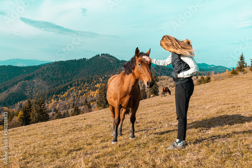 Cute girl with her horse in a beautiful meadow illuminated by warm evening light