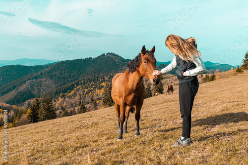 Portrait of cheerful, positive, young blond beautiful Caucasian woman with horse in countryside outdoors in autumn
