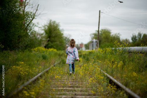 A little girl walks along the grassy railroad tracks. Ecology. The concept of the victory of nature over the vitality of man. Nature takes its toll.