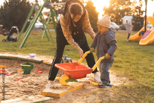 Mother and child playing with wheelbarrow in sandbox. Little builder. Education, and imagination, purposefulness concept. Support childhood parenthood symbol photo