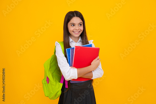 School teenage girl with school bag backpack hold book on yellow isolated studio background. Children school and education concept.