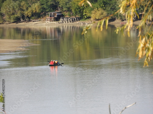 kayak with a crew of three kayakers on the surface of a wide river on a sunny autumn day