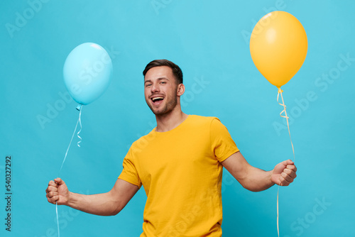 Cheerful happy friendly tanned handsome man in yellow t-shirt smile at camera hold balloons posing isolated on blue studio background. Copy space Banner Mockup. Friendship concept photo