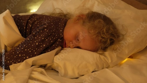 tooth fairy coin under pillow, milk tooth reward, cute cheerful girl sleeping on her bed, light under pillow photo