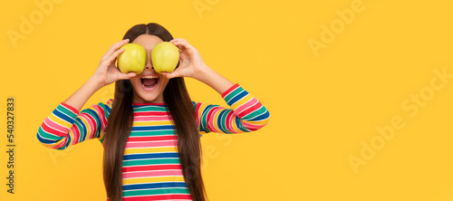Happy girl child have fun holding apple fruit at eyes yellow background, eye health. Child girl portrait with apple, horizontal poster. Banner header with copy space.
