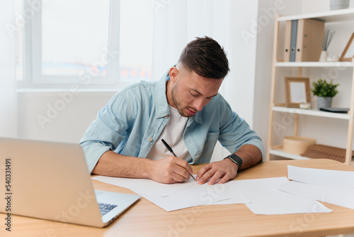 Serious focused good-looking young businessman signs important documents for work project in office. Copy space for ad. Remote Job, Technology And Career Profession Concept