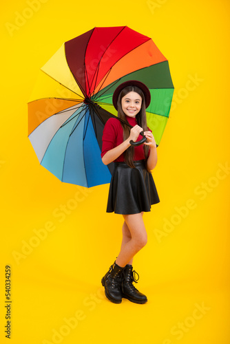 Happy teenager portrait. Teen girl with umbrella in autumn weather isolated on yellow background. Autumn kids clothes.