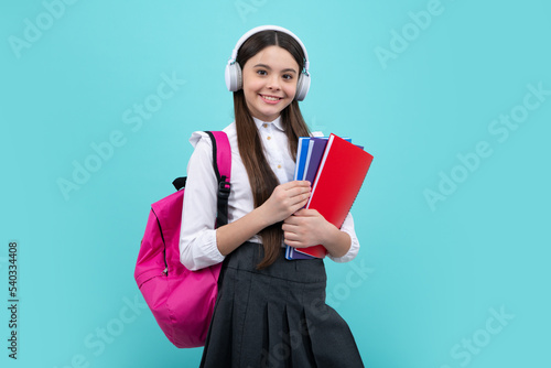 School girl, teenage 12, 13, 14 years old in headphones and books on isolated studio background. School kids with backpack.