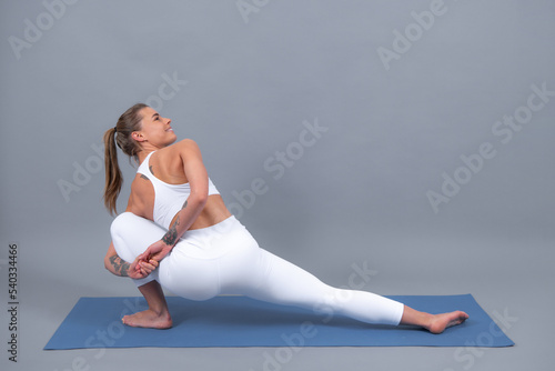 Sportive girl, during exercises on a yoga mat, raises her legs upward, gray background with space.
