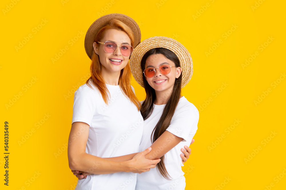 Happy stylish mother and daughter posing at studio yellow background, wearing straw hat and sunglasses. Summer family portrait. Happy stylish mother and daughter posing at studio yellow background, wearing straw hat and sunglasses. Summer family portrait.
