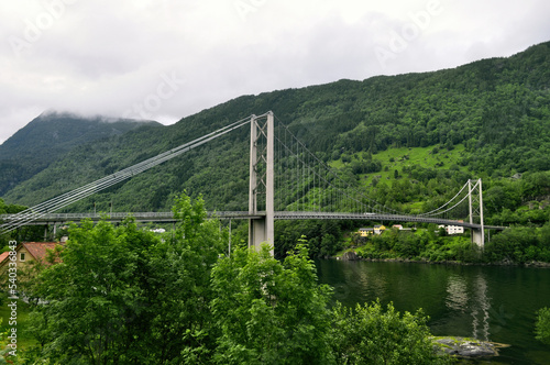 A large iron bridge for cars across a river between two mountains. Road through a fjord in Norway.