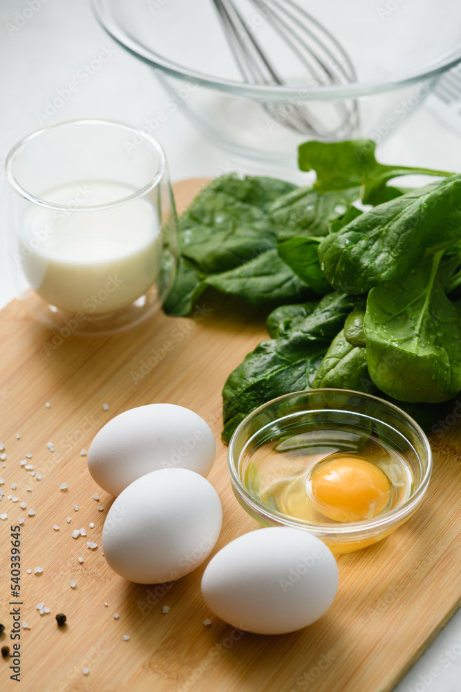 White chicken eggs on a cutting board with a bunch of fresh spinach. White chicken eggs on a cutting board with a bunch of fresh spinach.