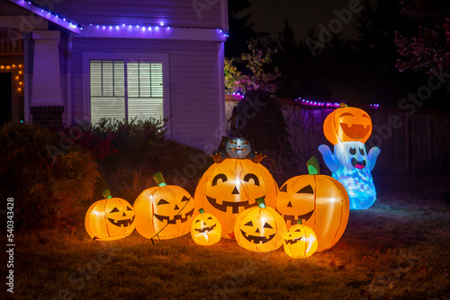 Illuminated night Halloween house outdoor decorations with inflatable figures of pumpkins, cat and ghost near house