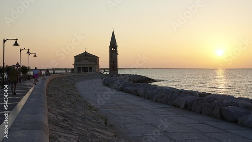Time lapse of people stroll at dawn on the seafront of Caorle, in the background the sanctuary 