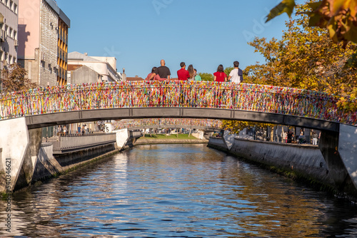Aveiro canal bridge with hanging Ribbons messages and a group of friends from behind standing on it, and the Ria Canal of Aveiro in the background. City of Aveiro, Portugal.