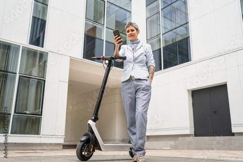 woman mature senior use mobile phone stand by electric kick scooter photo