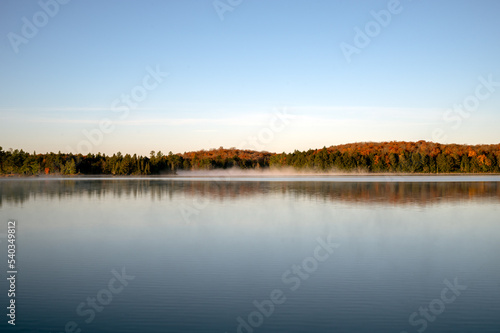 Autumn colored shoreline reflects on a calm lake. Rain Lake, Algonquin Provincial Park, Ontario, Canada.