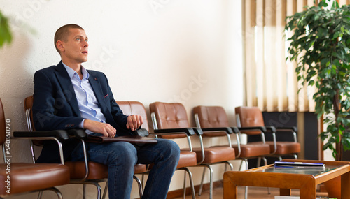 Portrait of young adult businessman sitting at hall in office, waiting for business meeting