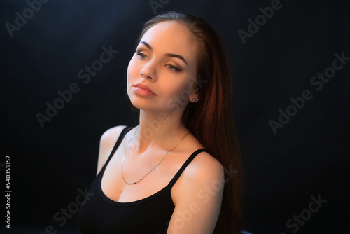 portrait of a beautiful young red-haired girl on a dark black background in the studio, with a cleavage and big breasts in black