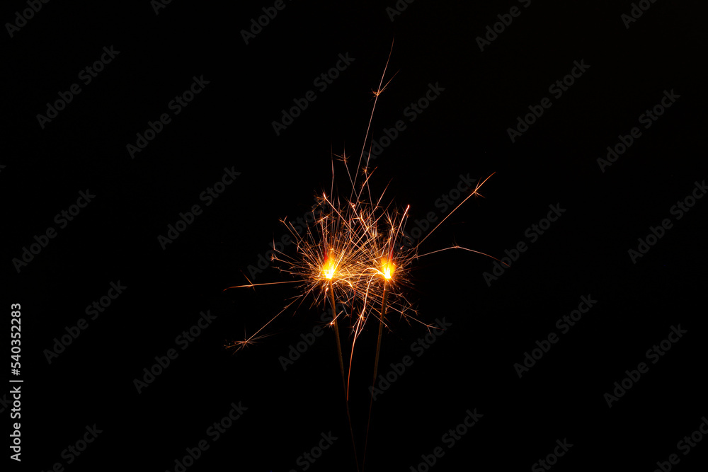 Two burning sparkler sticks on black background