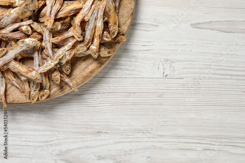 Plate of tasty dried anchovies on white wooden table, top view. Space for text