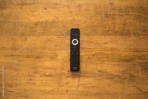 Television remote control on rustic wooden desk.