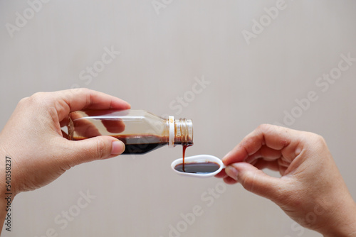 hand pours cough syrup, fever medicine and cold medicine containing paracetamol into a measuring spoon. photo