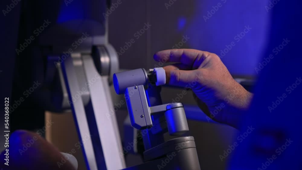 Managing the handles of futuristic surgical robot. Male doctor in blue uniform operates the high precise technological equipment Da Vinci. Managing the handles of futuristic surgical robot. Male doctor in blue uniform operates the high precise technological equipment Da Vinci.