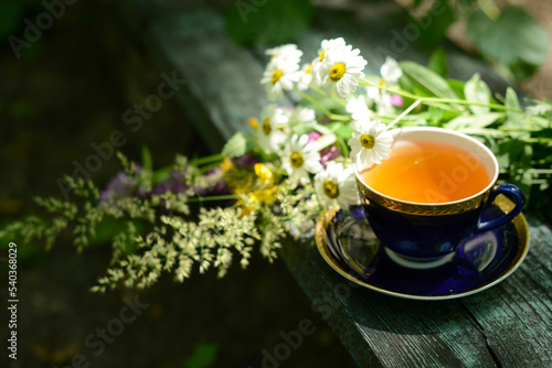 Herbal tea, cup of tea and bouquet chamomile flowers and wildflowers on wooden table in garden, blurred background, soft focus