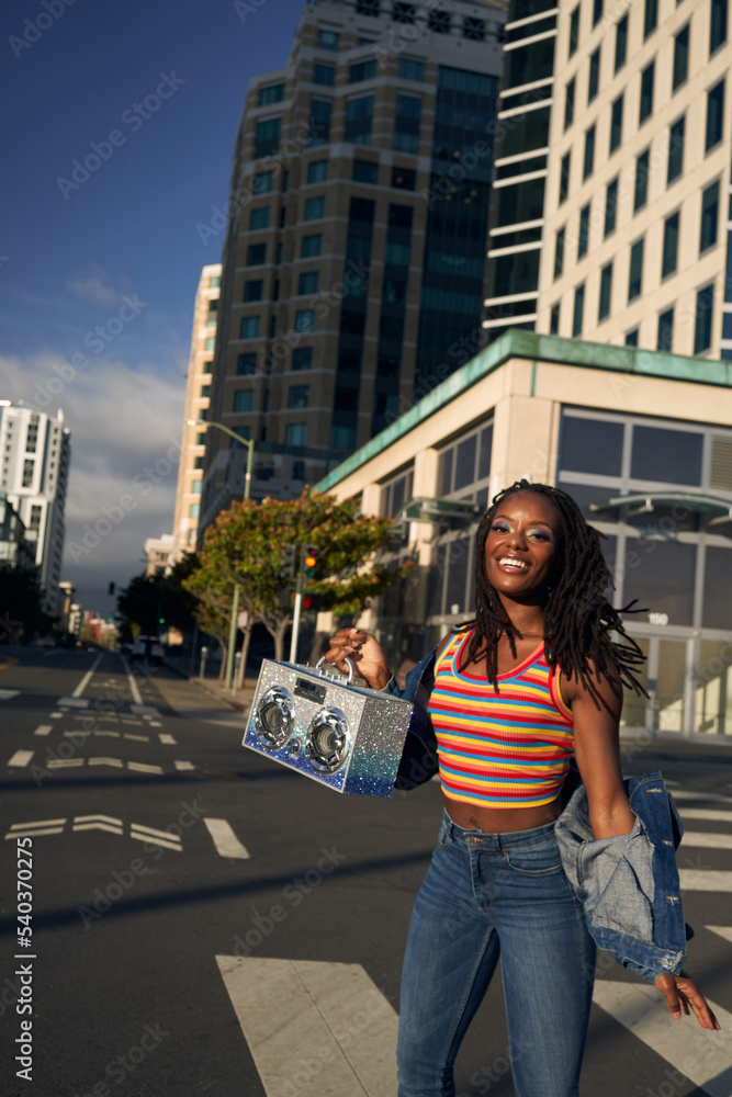 Portrait of young beautiful woman with dreads in the city smiling with boombox