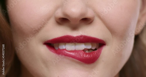 Studio macro close-up shot of woman flirting and biting lip with red lipstick makeup on, isolated on white studio background