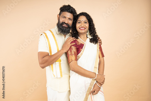 Portrait of happy south indian couple wearing traditional white dress isolated on beige background. photo