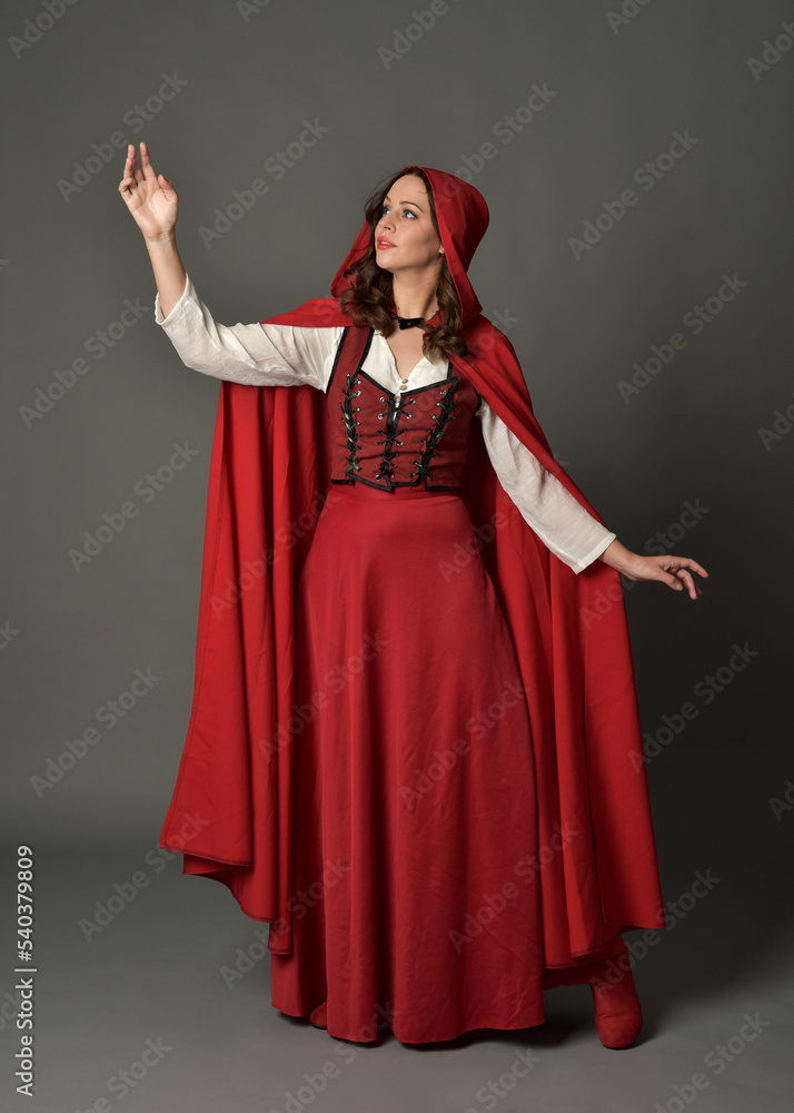 Full length portrait of beautiful brunette woman wearing red medieval fantasy costume with long skirt and flowing hooded cloak.
Standing pose with gestural hand poses, isolated on grey studio backgrou Full length portrait of beautiful brunette woman wearing red medieval fantasy costume with long skirt and flowing hooded cloak.
Standing pose with gestural hand poses, isolated on grey studio backgrou