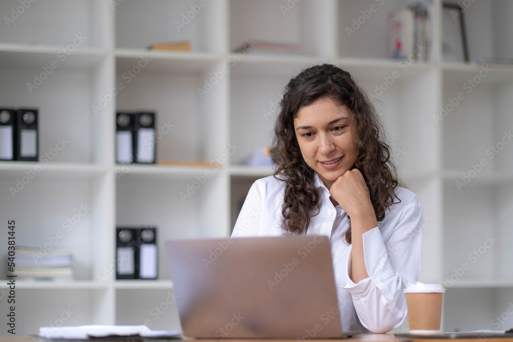 Photo of cheerful young woman working using computer laptop concentrated and smiling at office Photo of cheerful young woman working using computer laptop concentrated and smiling at office