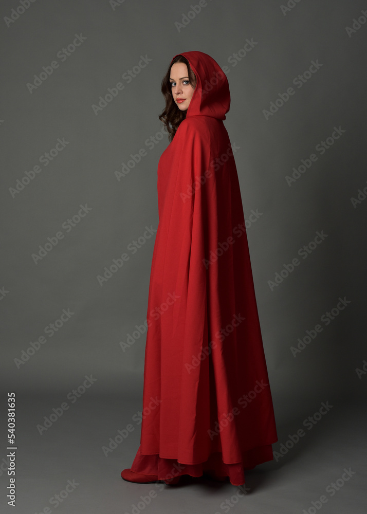 Full length portrait of woman wearing red medieval fantasy costume, flowing hooded cloak. Standing pose in backview, gestural hand poses, walking away from camera isolated on grey studio background. Full length portrait of woman wearing red medieval fantasy costume, flowing hooded cloak. Standing pose in backview, gestural hand poses, walking away from camera isolated on grey studio background.