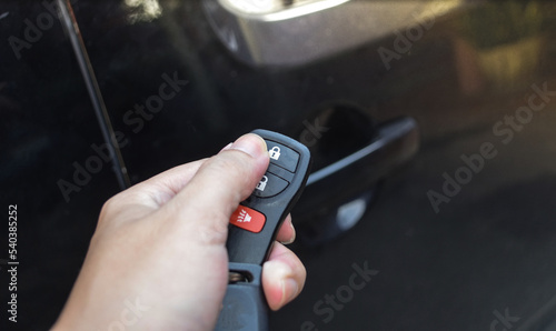 Close up hand of man holding and push car remote control for lock and Un-lock old black car ,Car key and  remote.