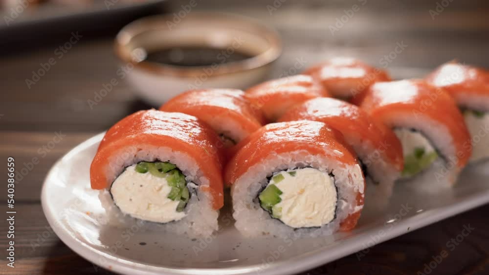 Eating Sushi with chopsticks. Philadelphia sushi roll japanese food in restaurant. Sushi roll with salmon, vegetables, soy sauce, close up. Japan menu Eating Sushi with chopsticks. Philadelphia sushi roll japanese food in restaurant. Sushi roll with salmon, vegetables, soy sauce, close up. Japan menu